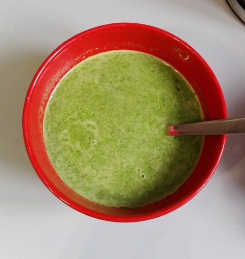 green spinach pesto and pea soup in a red bowl with spoon on kitchen worktop
