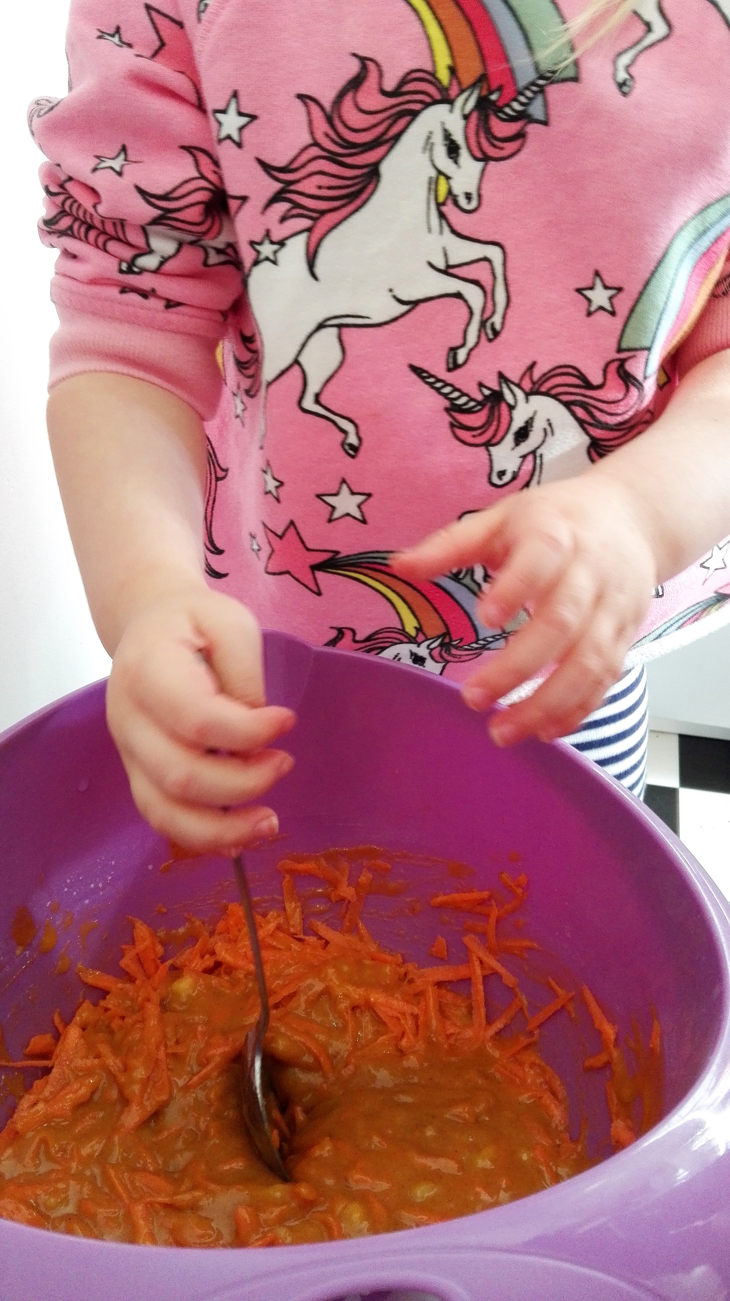purple mixing bowl with ingredients in being mixed by child