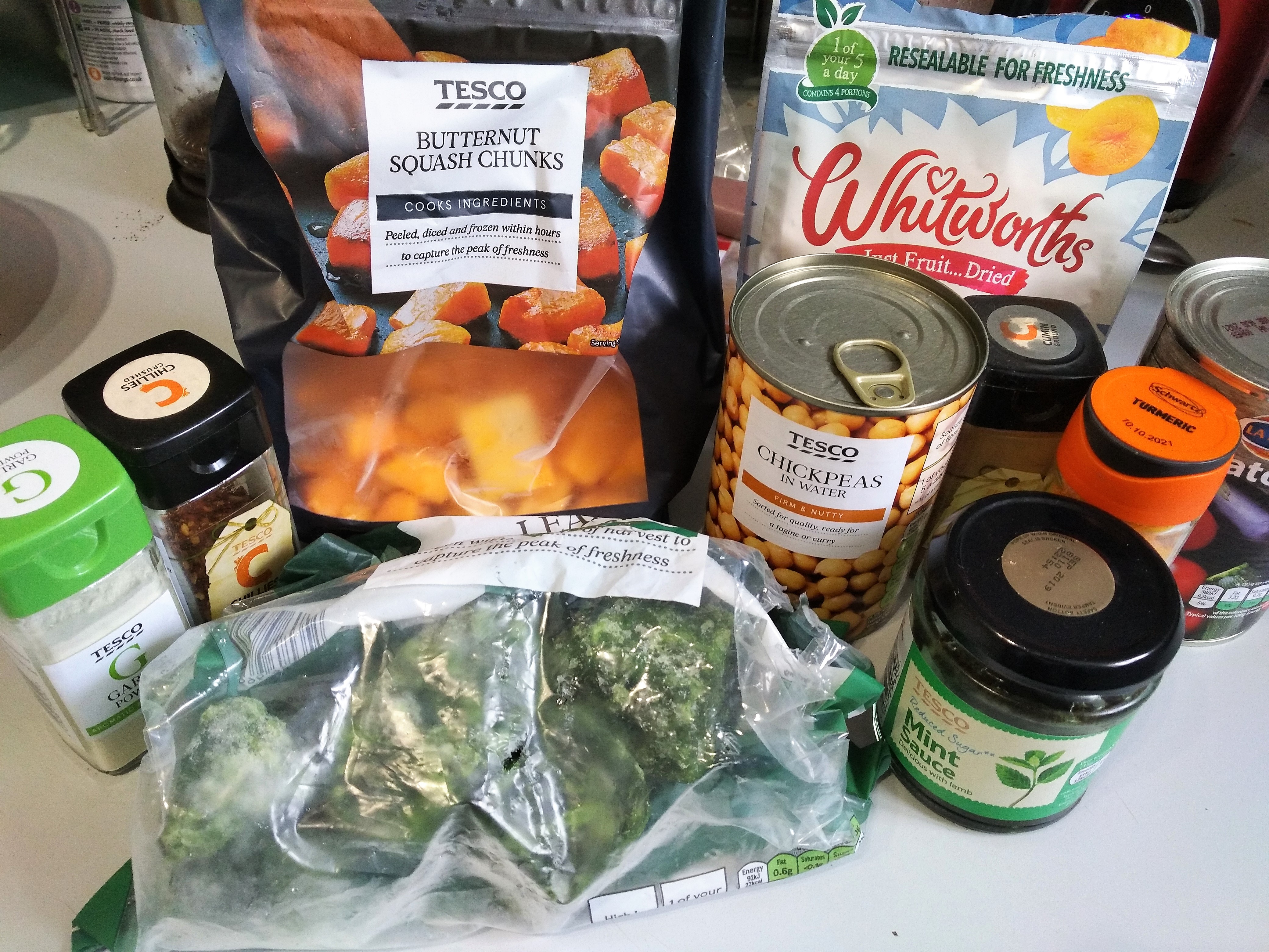 vegan moroccan tagine ingredients - garlic, crushed chillies, butternut squash chunks, tinned chickpeas, dried apricots, raisins, frozen spinach, cumin, turmeric, mint sauce and tinned ratatouille