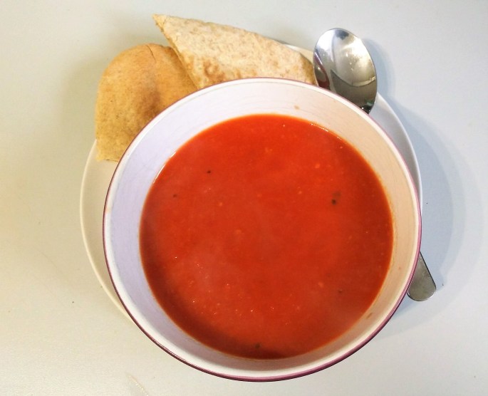 vegan tomato and ginger soup in a bowl on a plate with a spoon and a pitta bread