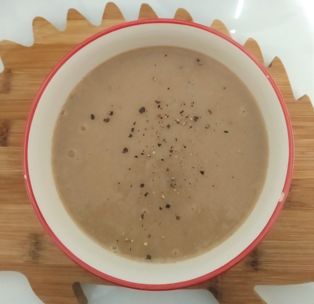 chestnut and parsnip soup in a white bowl on a brown hedgehog shaped chopping board. close up with black pepper