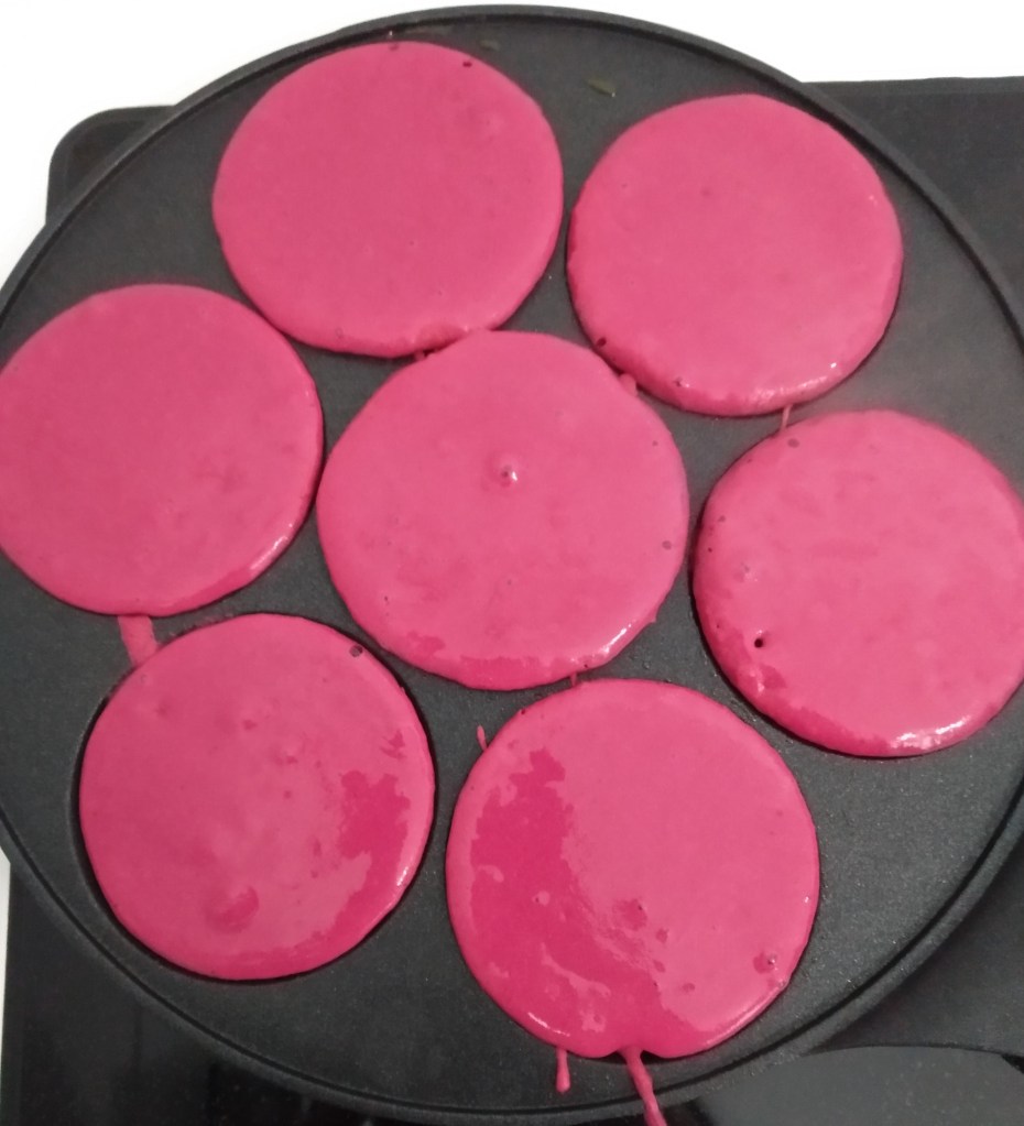 pink buckwheat pancake batter in a multi-hole frying pan for mini pancakes that are perfect for kids