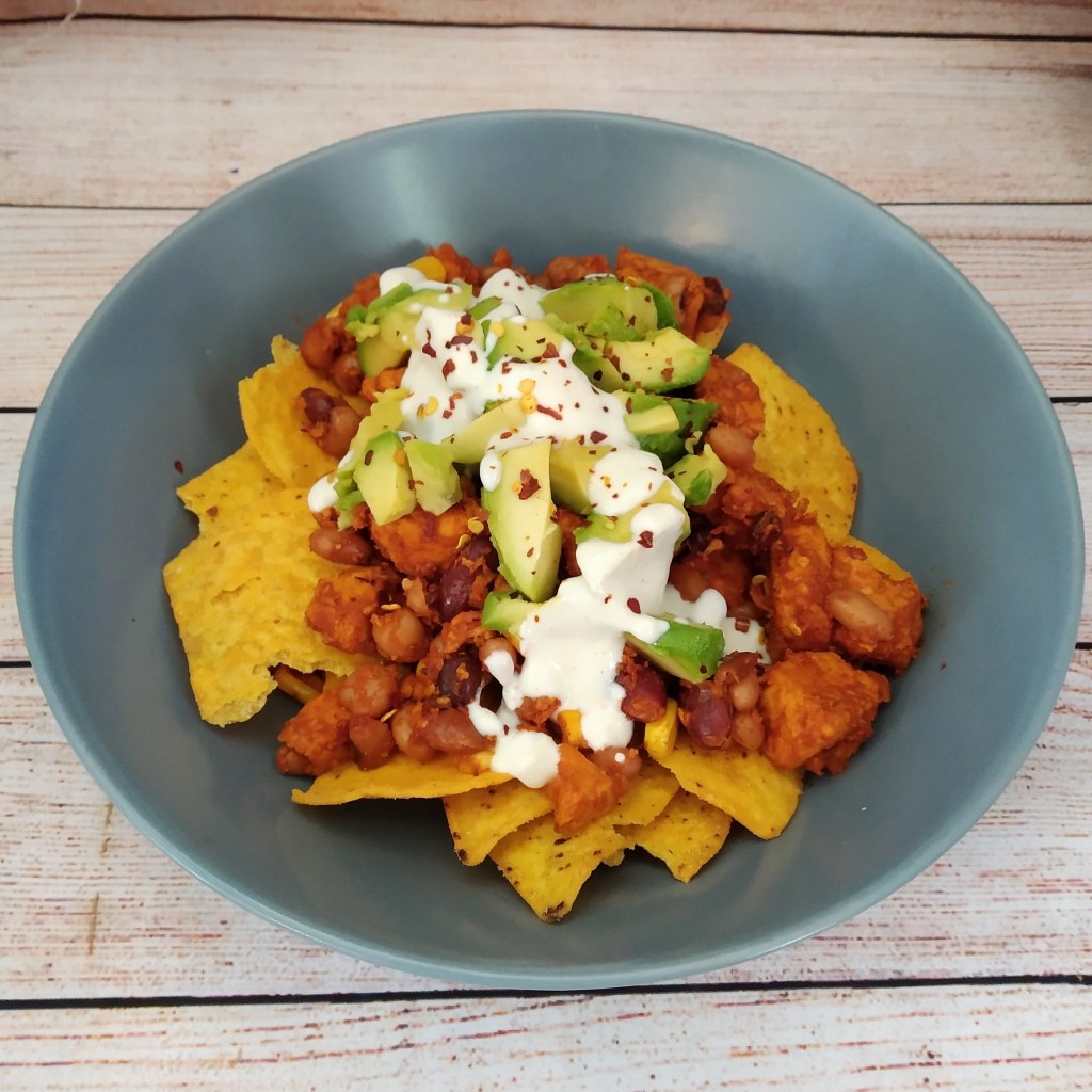 gluten free loaded vegan chicken nachos with avocado and dairy free sour cream in a grey bowl