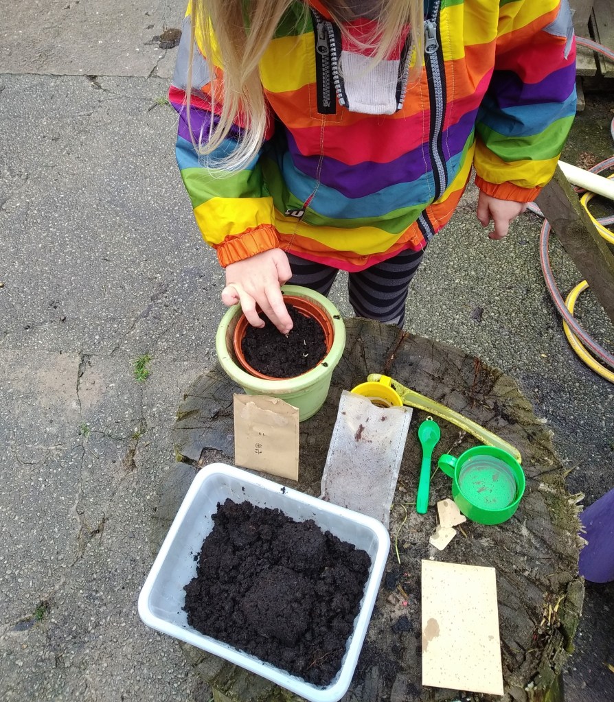 my home educated child in a rainbow coat planting seeds in a pot in the garden